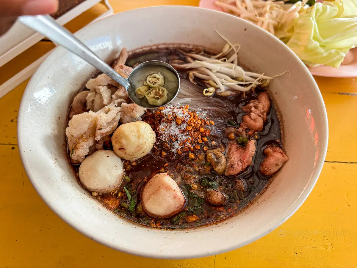 Adding prik nam som (Thai chilies in vinegar) to noodle soup.