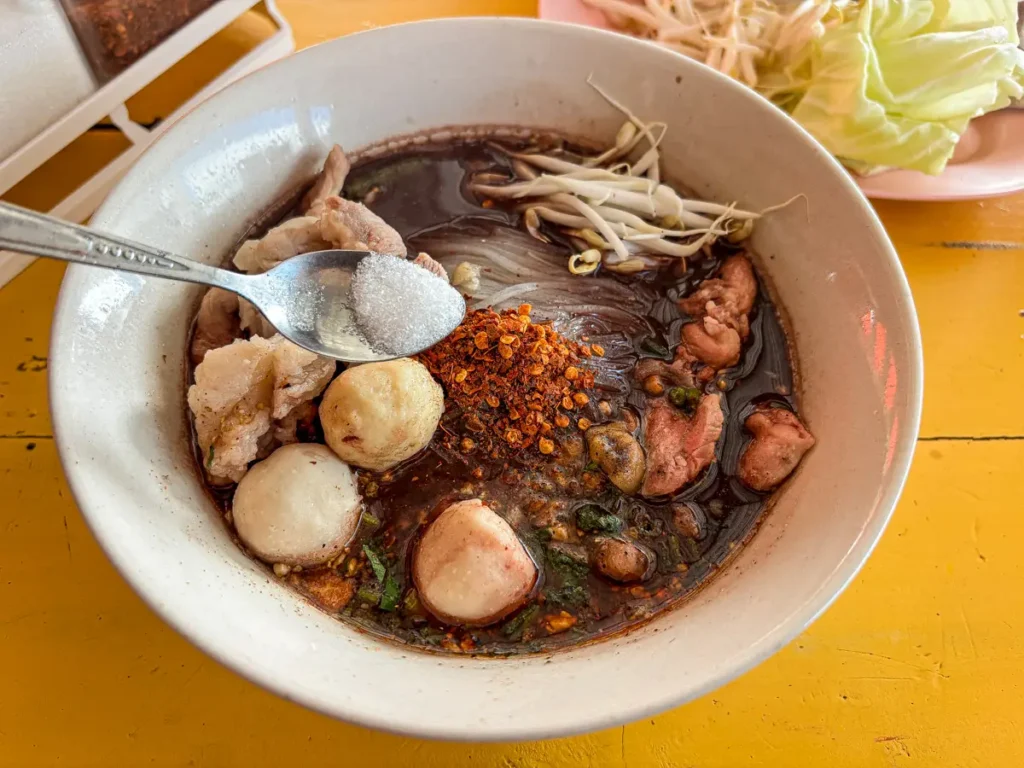 Adding sugar to Thai noodle soup.