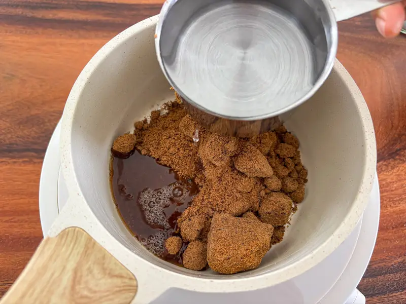 Adding water to brown sugar in a saucepan.