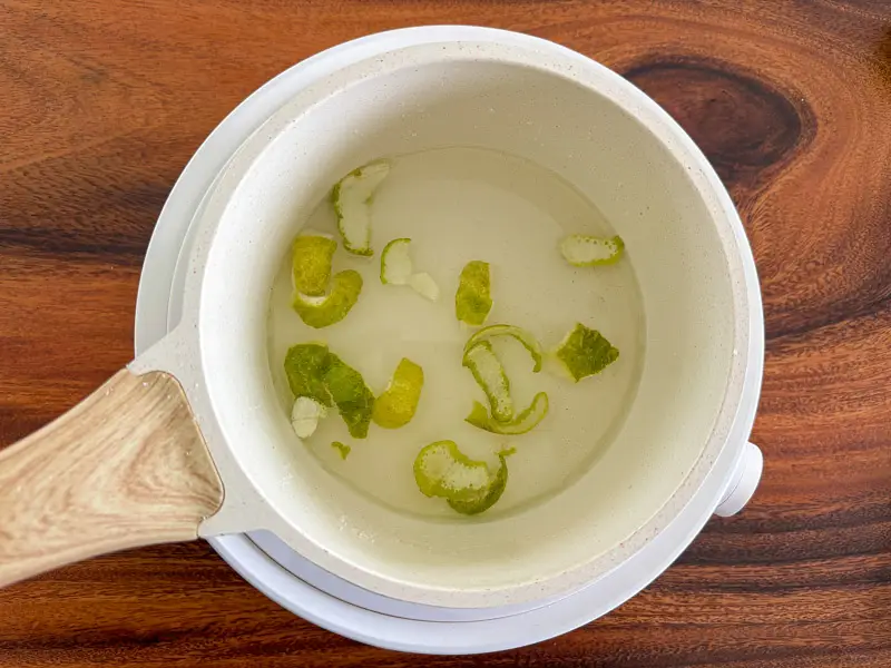 Adding water to lime peels in a saucepan.