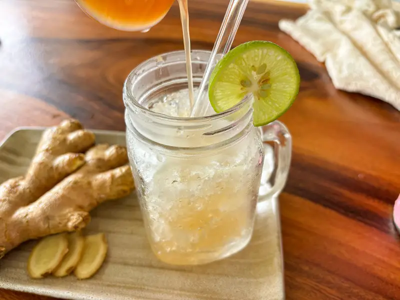 Pouring homemade ginger syrup into ginger soda with ice.