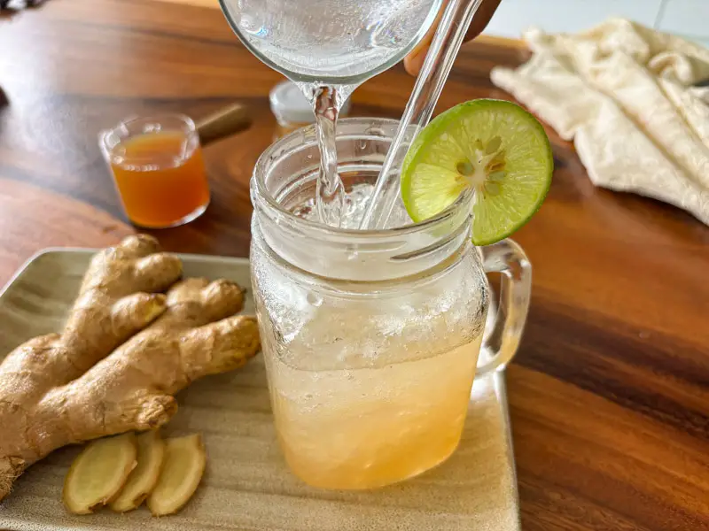 Pouring sparkling water into ginger soda with ice and lime.