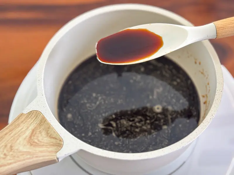 Checking the consistency of homemade brown sugar syrup with a spoon.