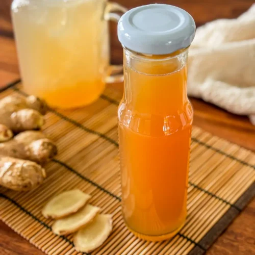 Homemade ginger syrup in a glass bottle with fresh ginger slices.