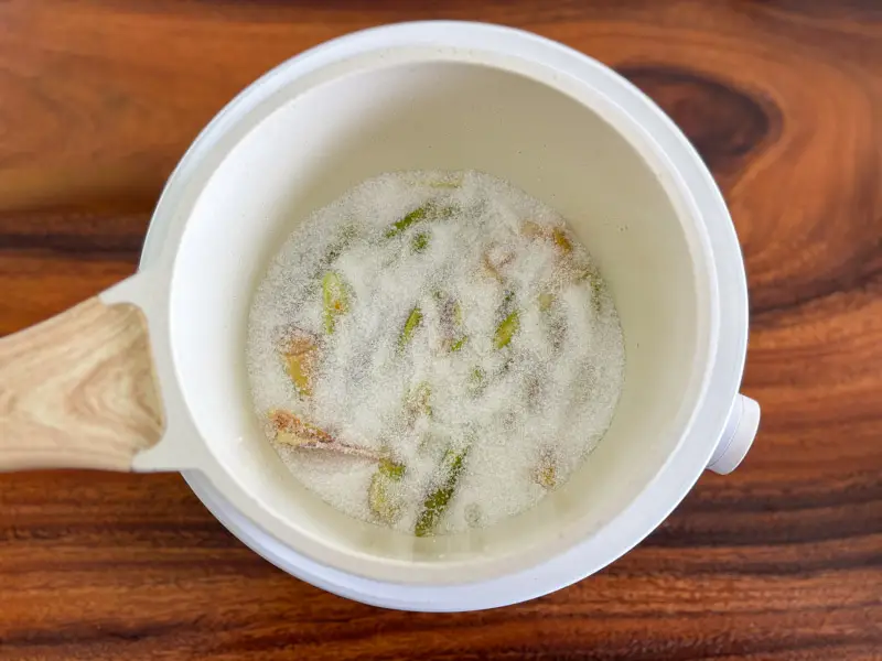 Sugar added to sliced lemongrass in a saucepan.