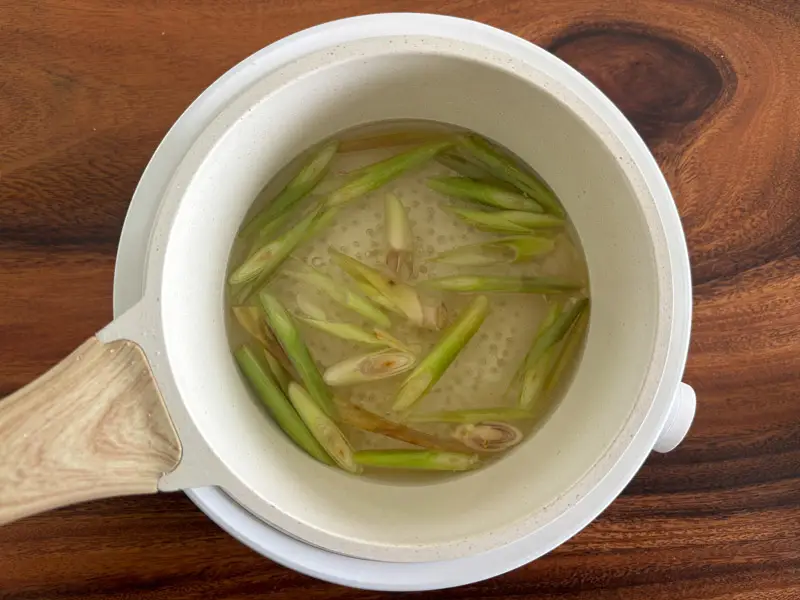 Sliced lemongrass simmering in sugar syrup.