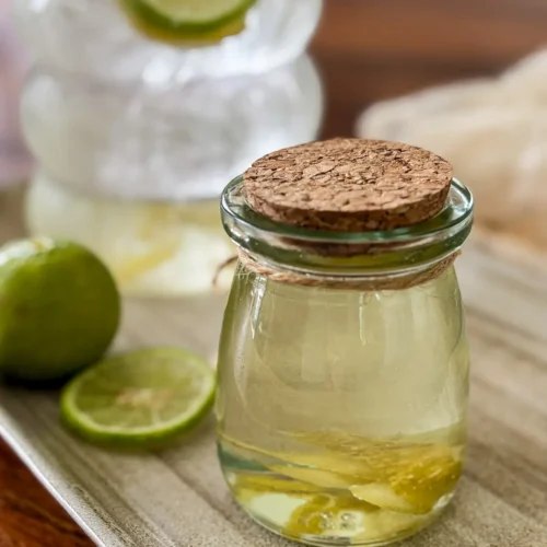 Homemade lime syrup in a glass jar with fresh lime slices.
