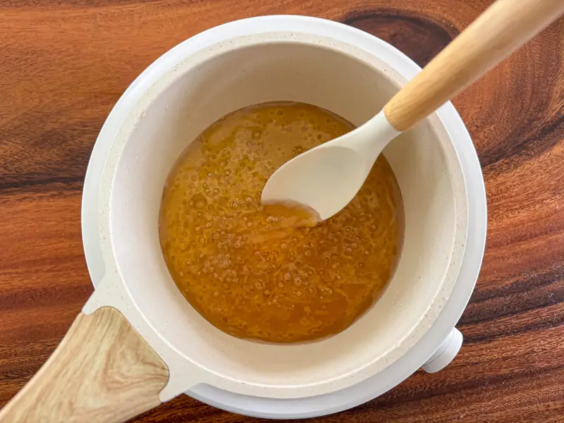 Stirring melted palm sugar to make homemade palm sugar syrup.